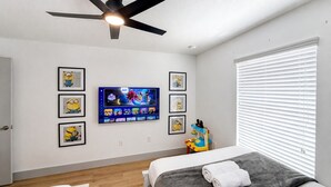 A bedroom with a bed, a ceiling fan, a TV mounted on the wall, and a window with blinds.