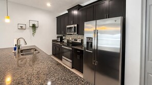 A modern kitchen with dark cabinets, stainless steel appliances, a granite countertop, and a built-in microwave. - 3 King Masters + Private Pool | 15 Min Disney (Kissimmee)
