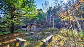 A rustic cabin with a fire pit and benches in a forest setting. - Pet-Friendly New York Cabin w/ Hot Tub & Game Room (Maplecrest)
