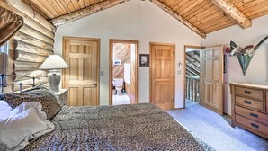A bedroom with a wooden ceiling, a bed with a leopard print blanket, a dresser, and a lamp. - Pet-Friendly New York Cabin w/ Hot Tub & Game Room (Maplecrest)