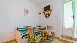 Uma sala de estar pequena com um sofá, duas cadeiras, uma mesa, uma televisão e uma porta com cortina verde.