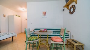 Um quarto pequeno e aconchegante com um sofá de riscas verdes, duas cadeiras, uma mesinha redonda e uma cama.