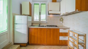 Uma cozinha compacta com armários de madeira, uma geladeira branca, um fogão a gás e uma janela com cortinas verdes.
