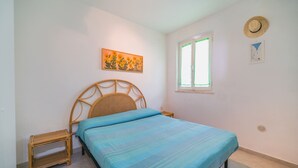 A bedroom with a bed, a nightstand, a window with a view, and a painting on the wall.
