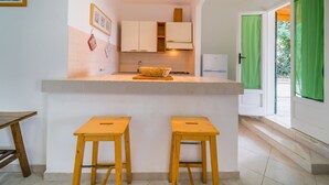 A compact kitchen with white cabinets, a central island with stools, and a view through green curtains.