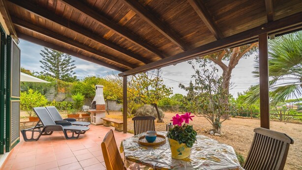 Un patio couvert avec une table dressée pour les repas, des sièges d’extérieur et un barbecue.