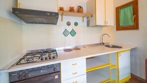 Une cuisine équipée d’une cuisinière à gaz, d’un four, d’un évier et d’étagères de rangement jaunes.