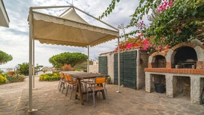 An outdoor patio with a table and chairs, a brick oven, and a pergola providing shade. - APPARTAMENTI RITA - MONO RITA N° 5 (Capoliveri)