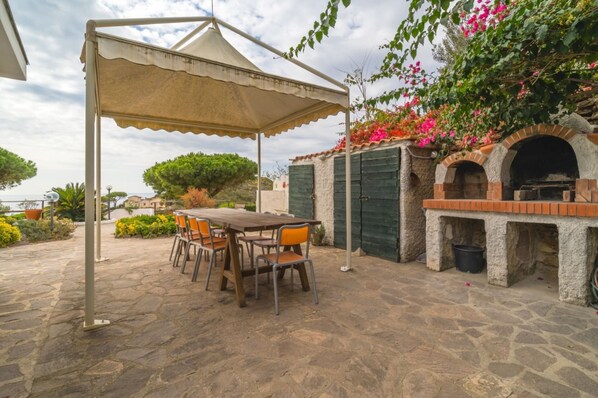 An outdoor patio with a table and chairs, a brick oven, and a pergola providing shade.