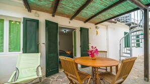 A covered outdoor seating area with a table and chairs, a green chair, and a flower vase. - APPARTAMENTI RITA - MONO RITA N° 5 (Capoliveri)