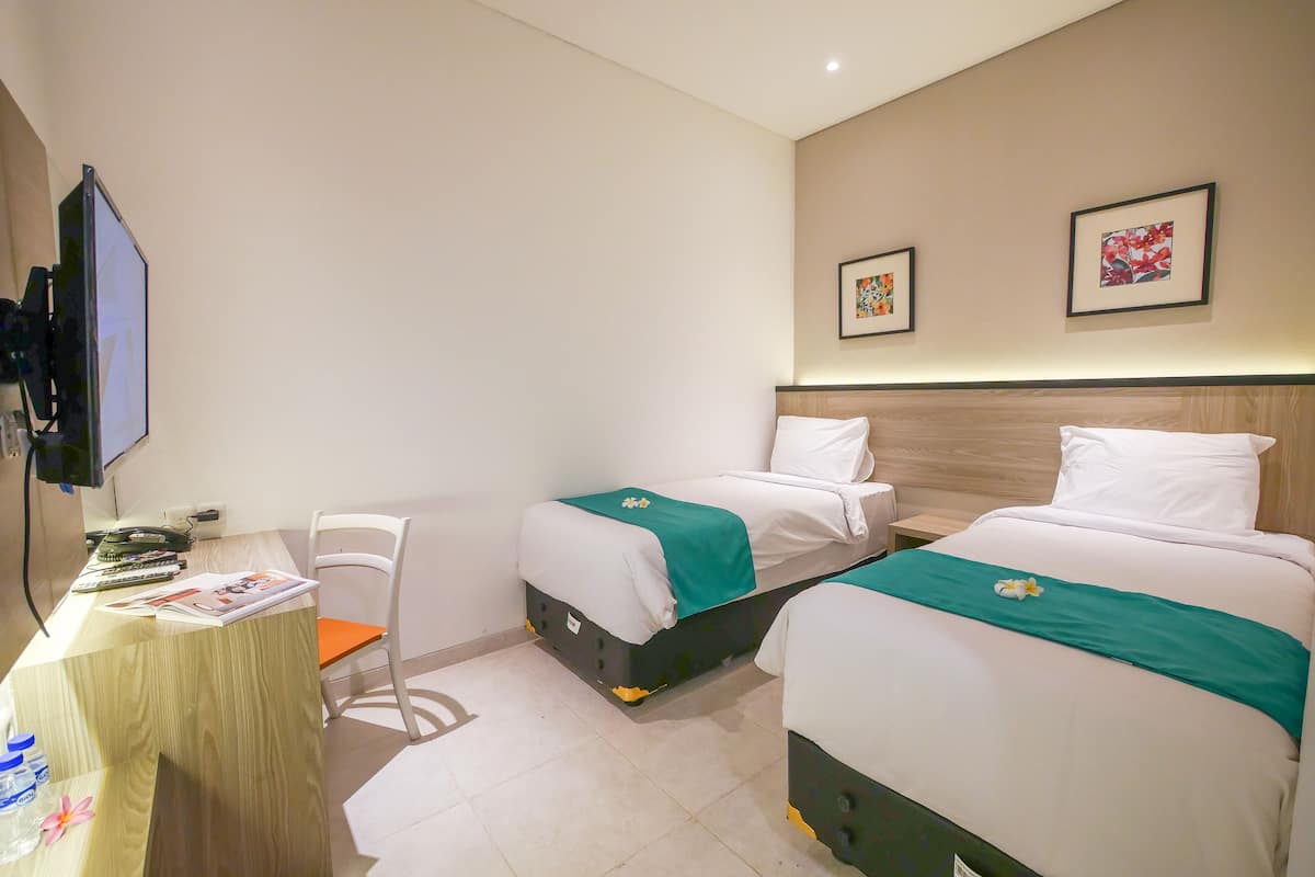 Een hotelkamer met twee bedden, een bureau met stoel, een televisie en kunst aan de wanden.