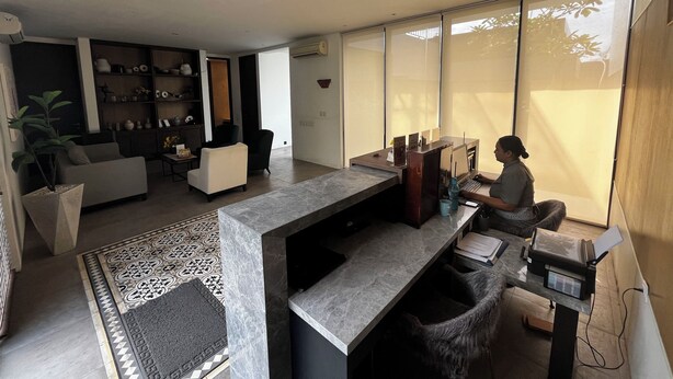 Un salon moderne doté d’une grande fenêtre, d’un bureau avec un ordinateur portable et d’un coin salon comprenant un canapé et des fauteuils.