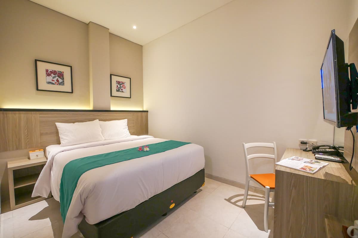 Een hotelkamer met een bed, een bureau met stoel, een televisie en twee ingelijste foto's aan de muur.