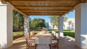 Een terras buiten met een houten pergola, een eettafel en stoelen.