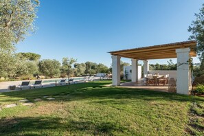 A covered outdoor area with a pool, lounge chairs, and a dining table.