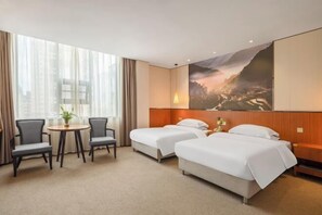 Una habitación de hotel con dos camas, una mesita con sillas y un ventanal con cortinas.