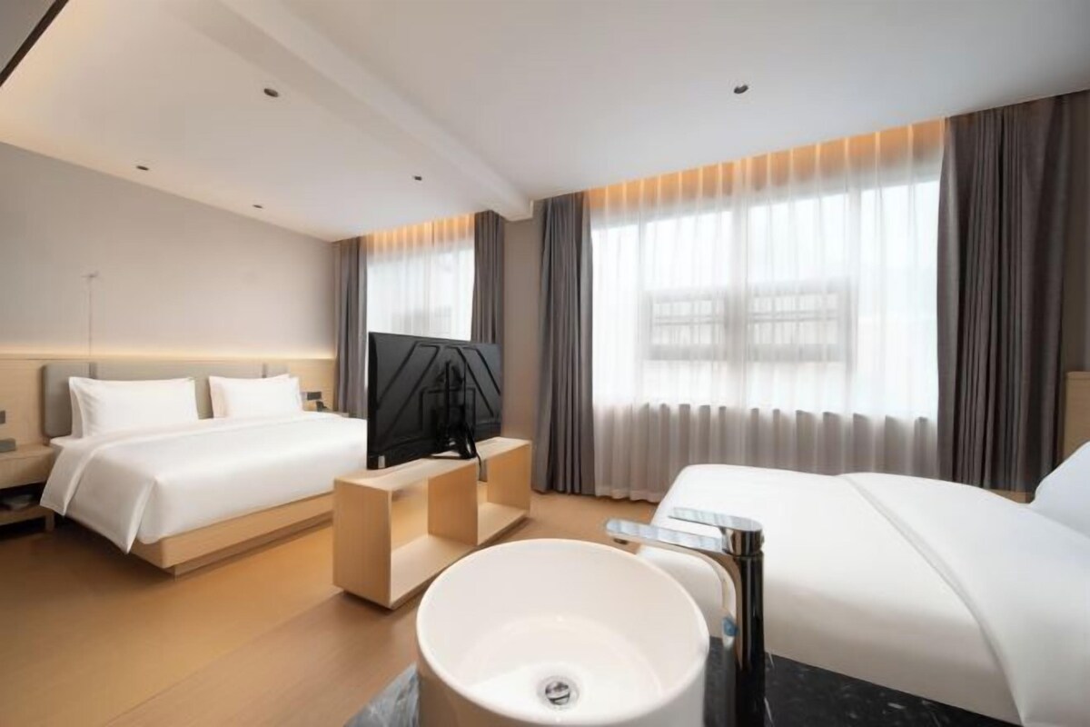 A hotel room with two beds, a TV, a large white sink, and a window with curtains.