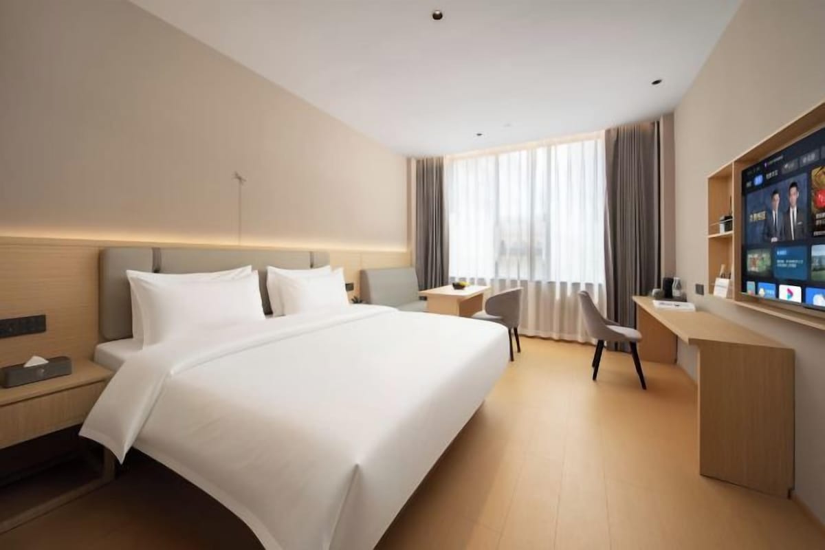 A hotel room with a large bed, a desk, and a TV.