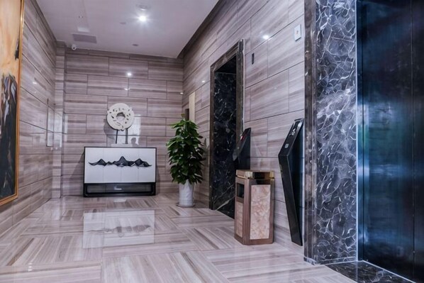 A modern lobby with a marble floor, a white console table with a plant, and a black elevator door. - Mini Hotel (Huaihua)