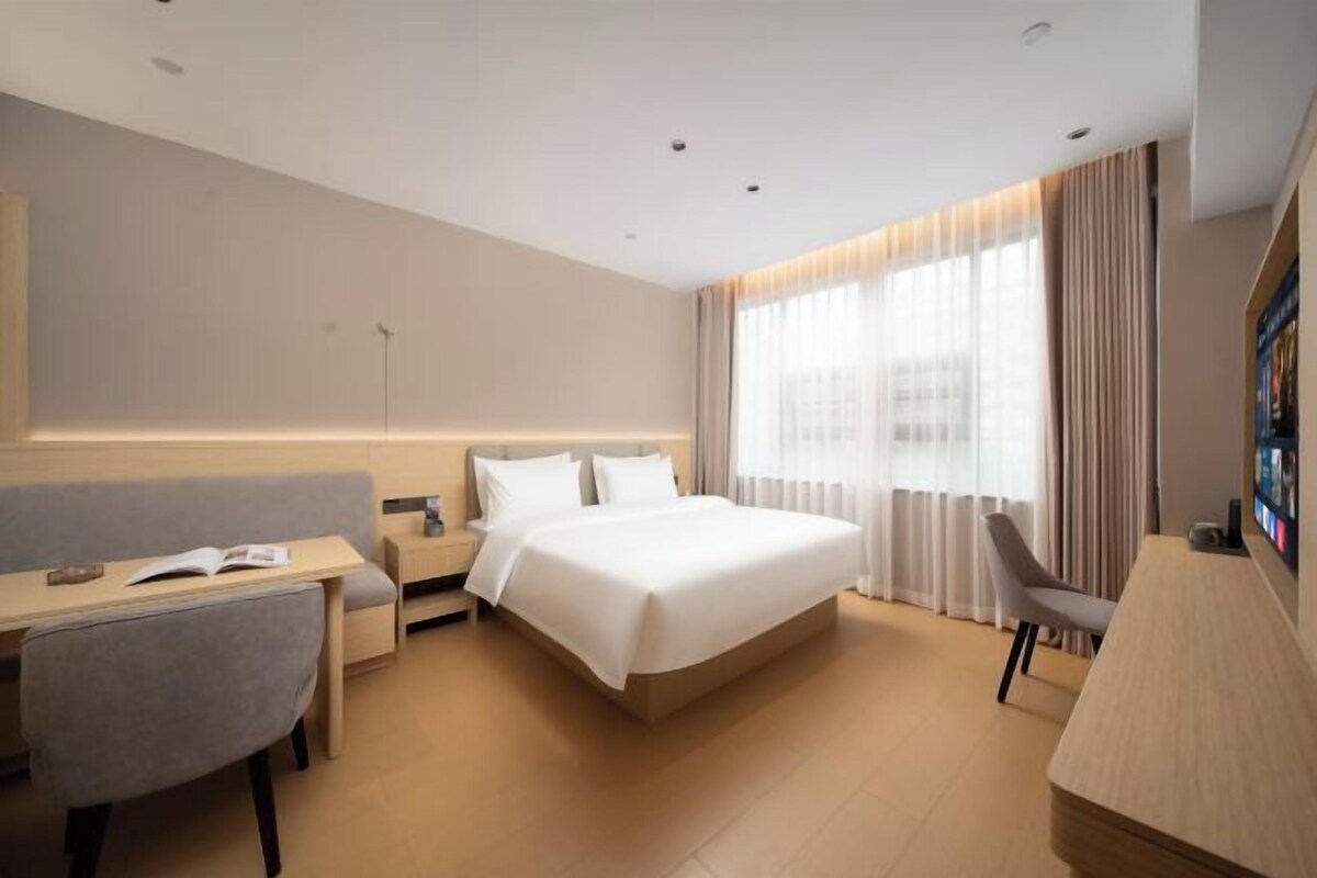 A modern hotel room with a bed, desk, chair, and a large window with curtains.