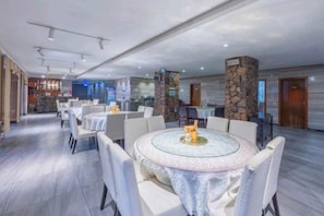Un hall d’hôtel spacieux, avec des tables et des chaises rondes, un coin bar et un pilier en pierre.
