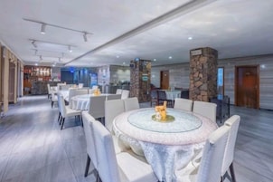 A spacious hotel lobby with round tables and chairs, a bar area, and a stone pillar.