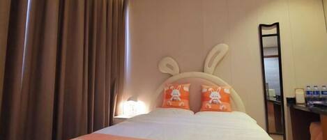 A hotel room with a bed, curtains, a headboard with bunny pillows, a bedside table with a lamp, and a mirror.