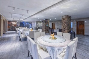 A modern hotel dining area with round tables, comfortable seating, and a stone pillar.