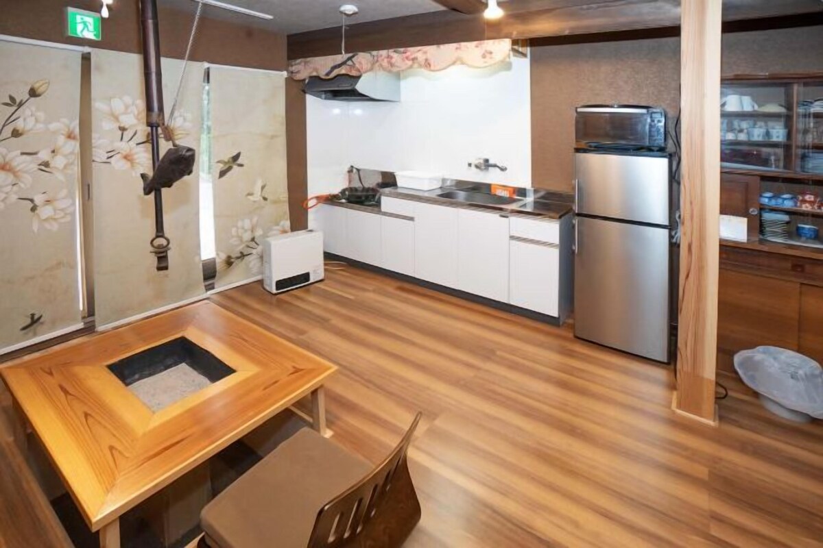 A compact kitchen with a wooden table and chairs, a refrigerator, and a microwave.