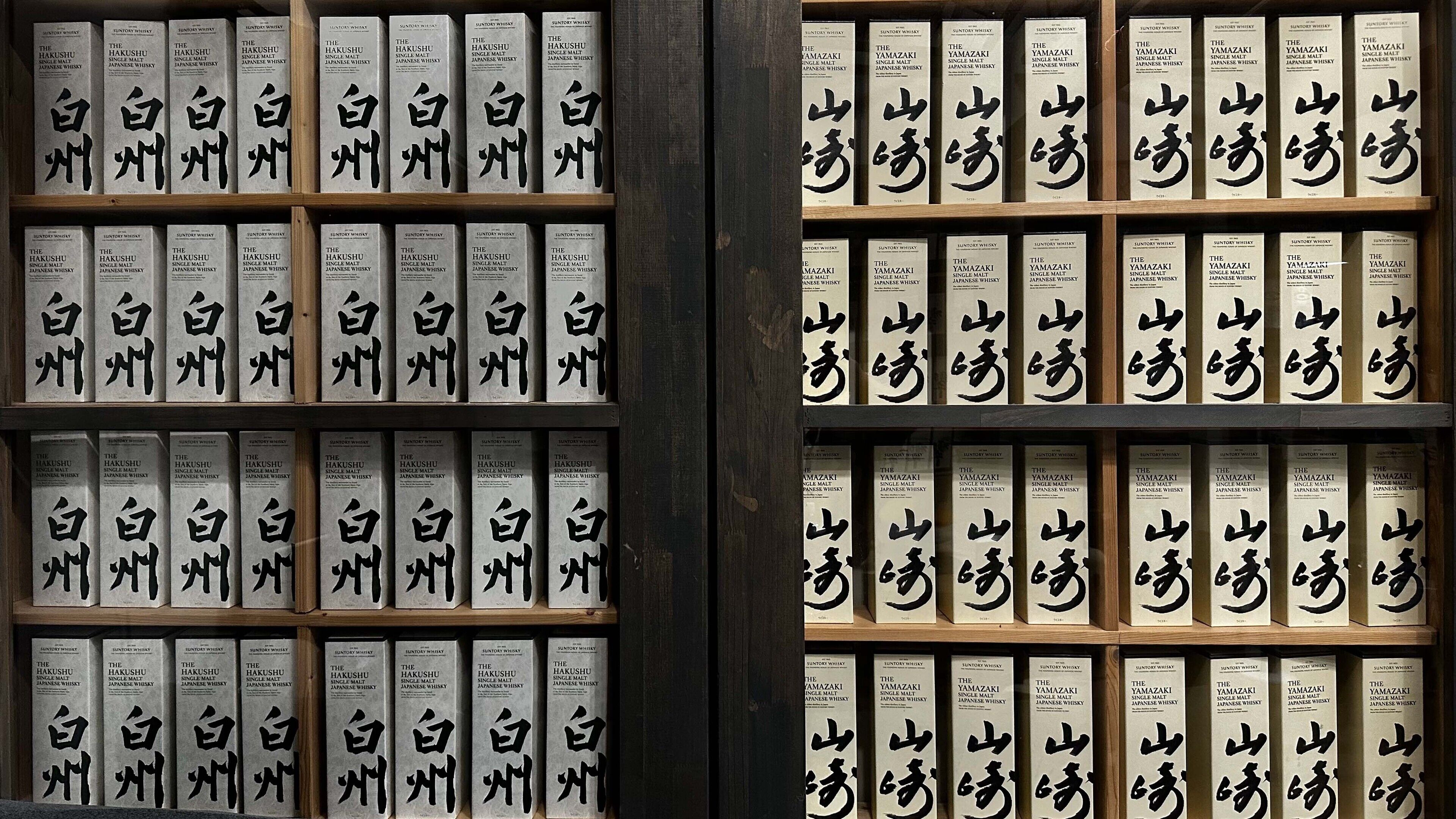 En utställning med whiskyflaskor, där etiketterna har japanska tecken, och som är uppradade i hyllor av trä.