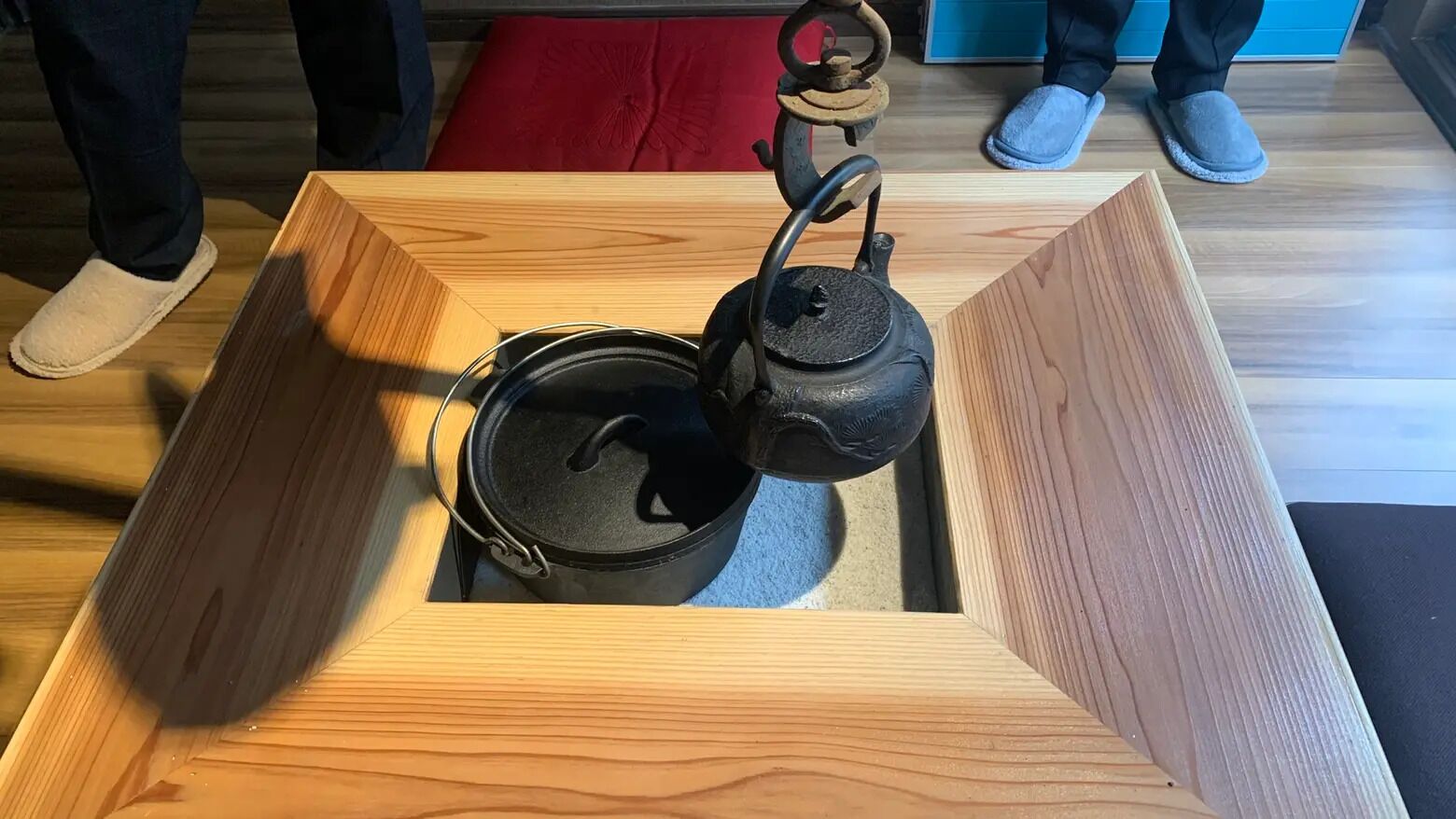 A wooden box with a black kettle inside, placed on a wooden floor.