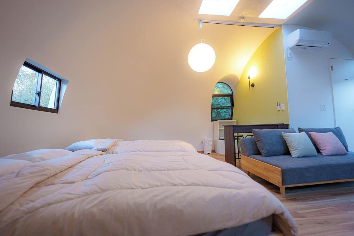 A bedroom with two beds, a sofa, a skylight, and a wall-mounted air conditioner.