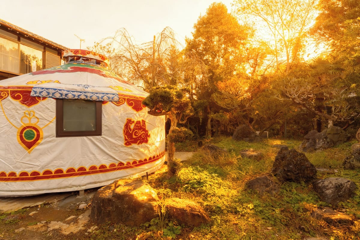 A traditional yurt with a decorative design, situated in a natural setting with trees and rocks.