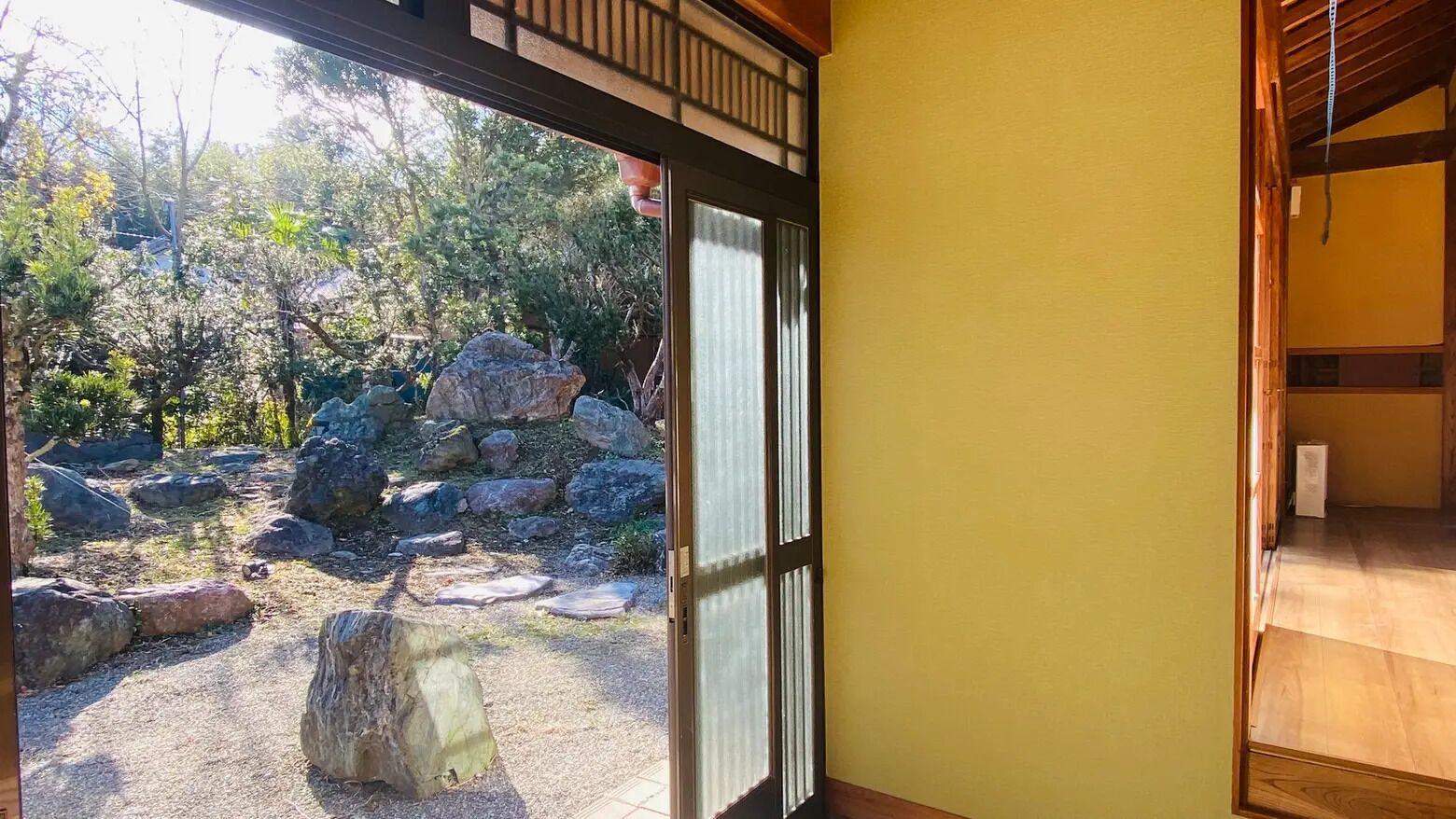 A traditional Japanese room with tatami flooring, a sliding door leading to a garden with rocks and trees.