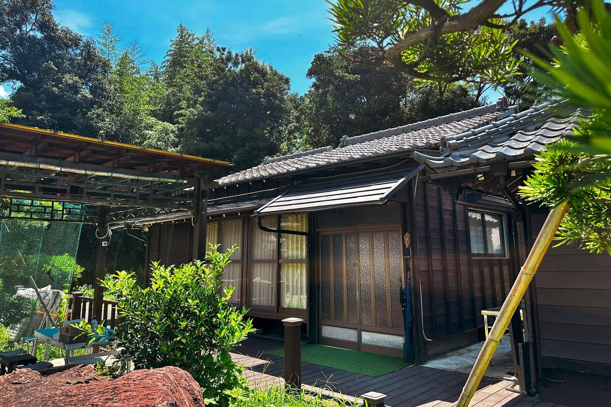 A traditional Japanese-style building with a tiled roof and wooden walls, surrounded by greenery and a wooden deck.
