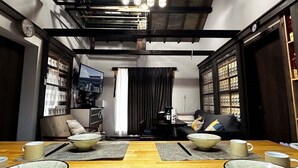 Una habitación tradicional japonesa con esteras de tatami, una mesa baja con cuencos de cerámica, un televisor y una estantería con libros y objetos decorativos.