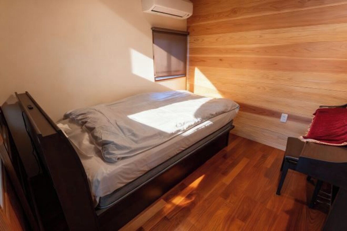 A small, single-bed room with a wooden floor and a window with blinds.