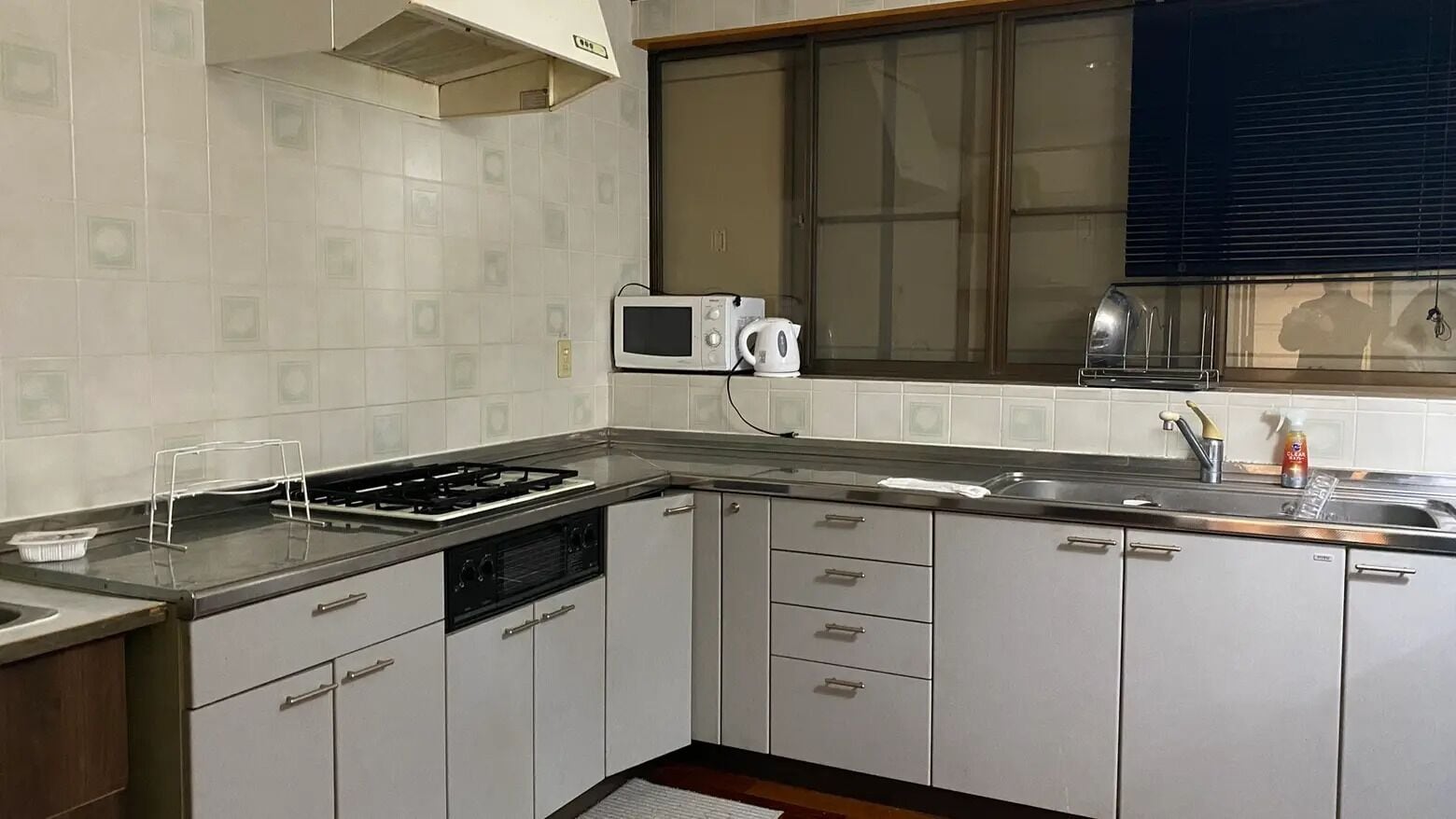 Een keuken met witte kastjes, een magnetron, een waterkoker en een broodrooster.