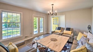 A spacious living room with a large wooden coffee table, comfortable seating, and large windows offering a view of the outdoors. - Mod 'Stable House' on 10 Acres, Walk to Lake! (Oakwood)