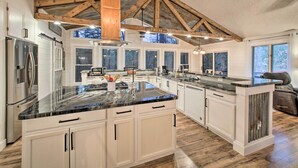 Een ruime keuken met een groot eiland, witte kastjes en een houten plafond.