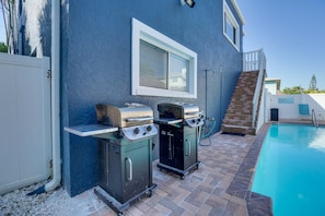 An outdoor barbecue area with two grills, a pool, and a staircase leading to a covered deck.