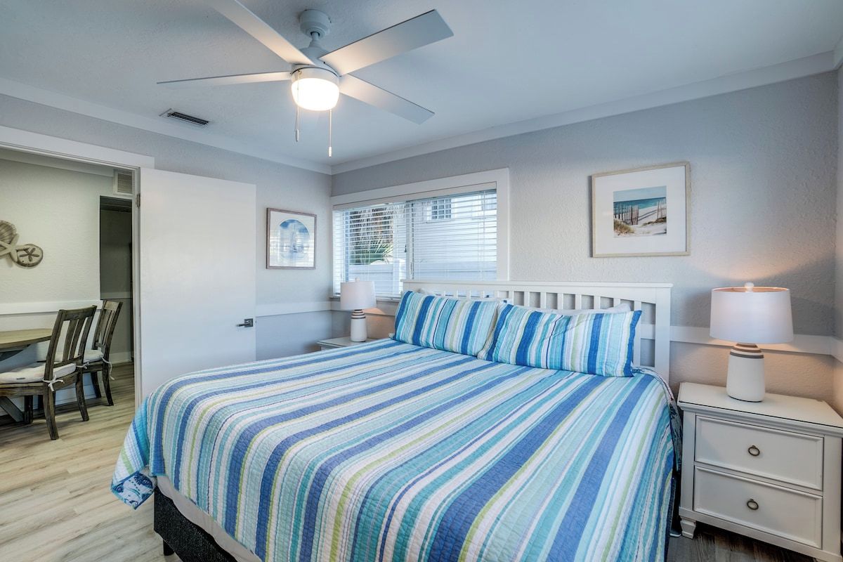 A bedroom with a bed, a nightstand, a ceiling fan, and a window with blinds.