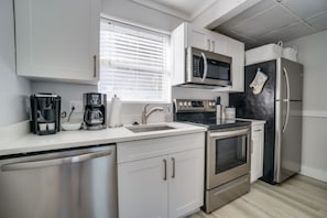 A modern kitchen with stainless steel appliances, a coffee maker, and a window with blinds.