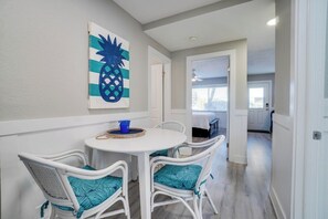 A dining area with a round table and four white wicker chairs, each with a teal cushion. A pineapple artwork is on the wall above the table. - Seagrass Flats Unit 1 (Bradenton Beach)