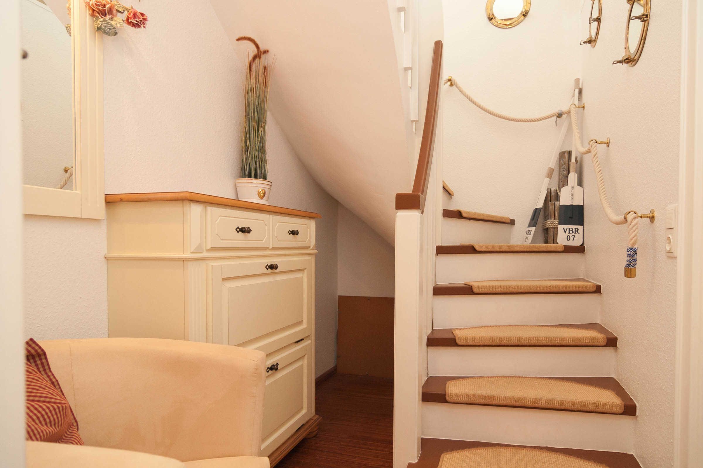 A staircase with a wooden handrail and a white wall with a mirror and a potted plant.