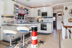 A kitchen with white cabinets, a central island with bar stools, a lighthouse decoration, and a view into the dining area. - Rüm Hart, Whg.18, Germany (Hörnum (Sylt))