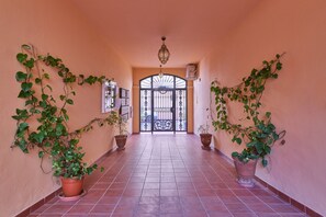 A corridor with potted plants on either side, a tiled floor, and a decorative gate at the end.