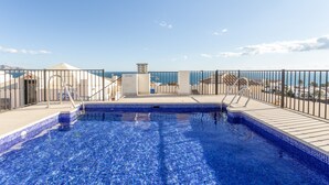 En pool på taket med fri utsikt över havet, omgiven av ett metallräcke och en plattbelagd terrass.