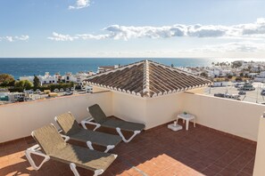 Eine Dachterrasse mit zwei Liegestühlen, einem kleinen Tisch und Blick auf das Meer und die Gebäude.