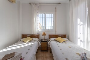 A bedroom with two beds, a nightstand, a lamp, and a window with bars.